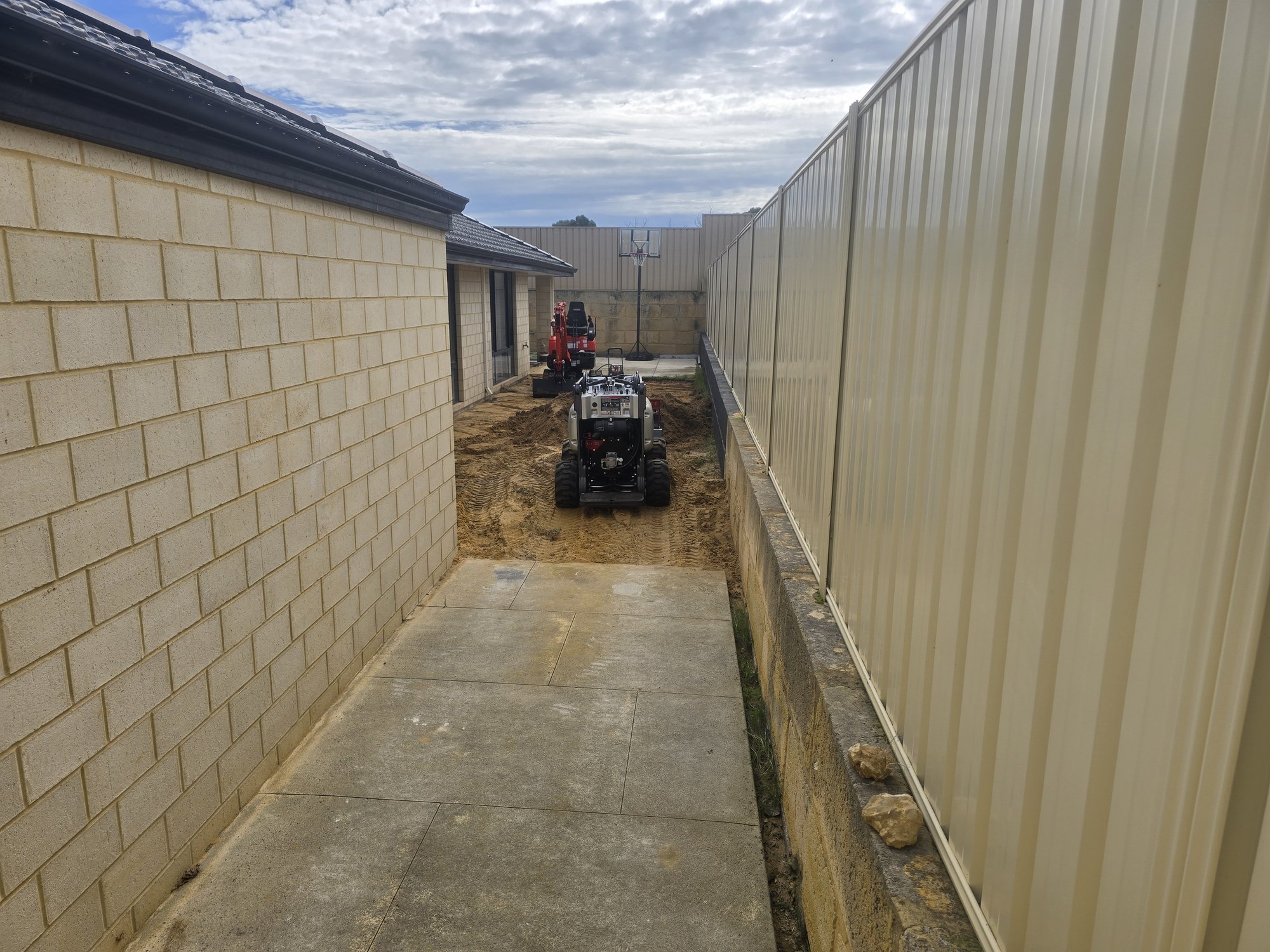 Machinery navigating the tight-access corridor between the house and boundary fence.